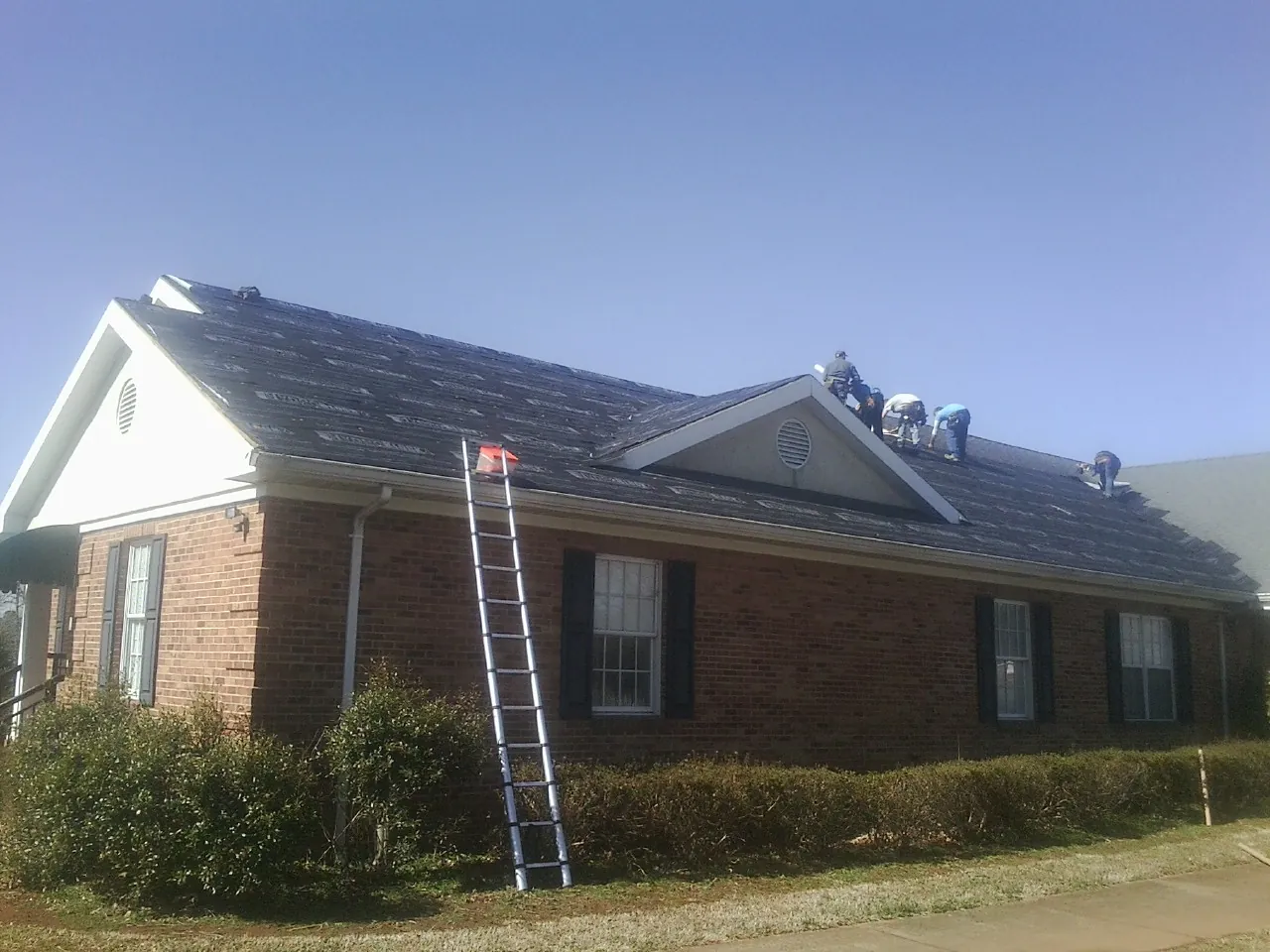 Crew tearing shingles off a brick ranch roof with a ladder set — Emergency Roof Repair work by our crew in Carrollton